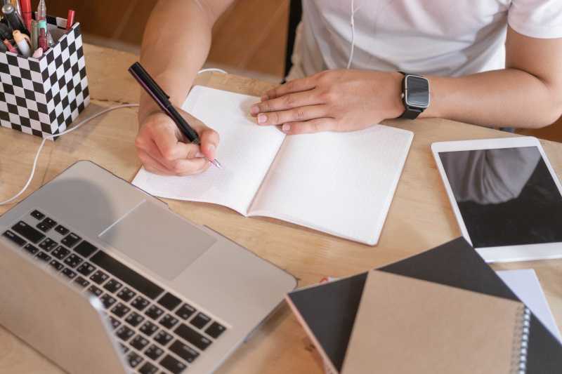 A person is writing at a desk with their laptop. 