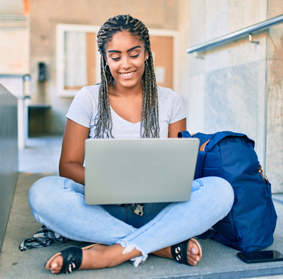 A young woman is sitting outside working on her laptop. 