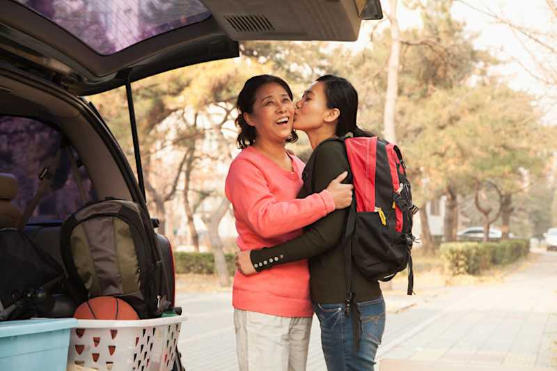 A mom and daughter at the back of a packed car hugging and kissing. 