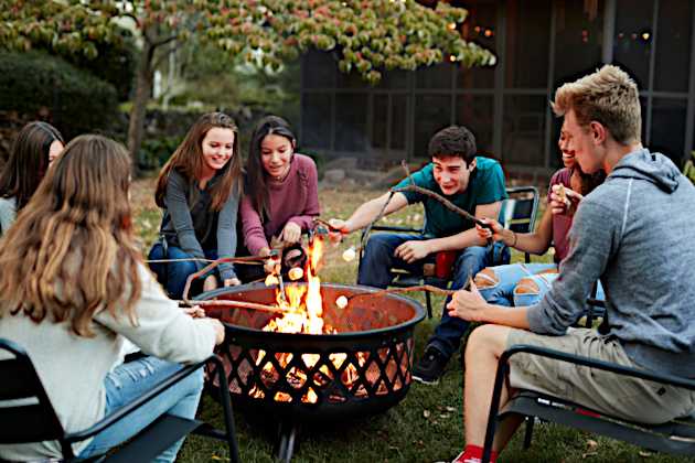 A group of teenagers are roasitng marshmallows around a campfire. 