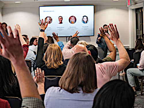 A classroom of people is at a presentation asking questions. 