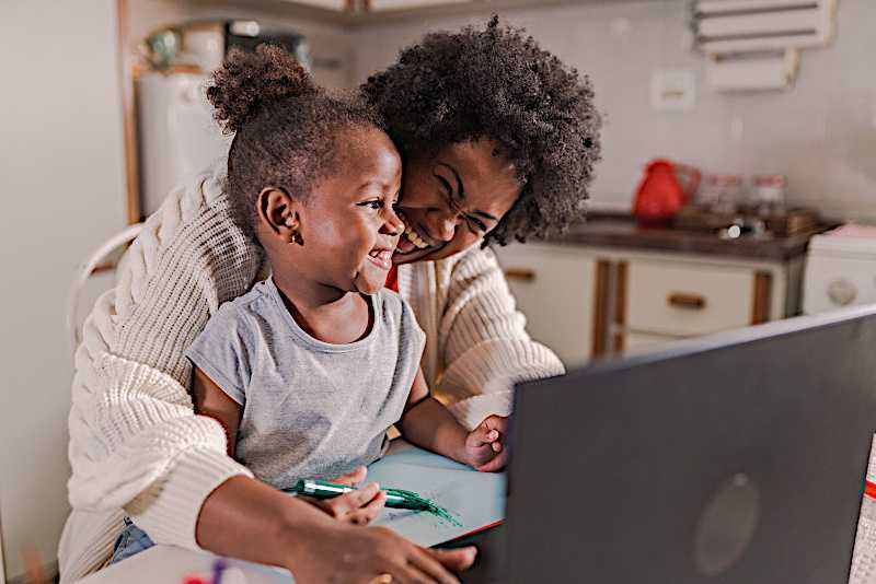 A toddler girl is sitting on her mom's lap in front of a laptop. 