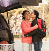 A mom and daughter embrace outside a car filled with belongings. 